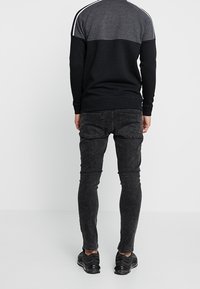 Felpa a blocchi di colore nero e grigio con strisce bianche sulle spalle, abbinata a jeans neri a gamba stretta e scarpe nere.