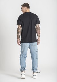 Černé bavlněné tričko s kulatým výstřihem, v kombinaci se světle modrými cargo kalhotami s bočními kapsami a elastickými manžetami, doplněné o bílé tenisky.