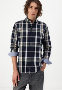Marineblaue Karoshemd mit weißen, grauen und gelben Akzenten; lange Ärmel mit hochgekrempelten Manschetten. Durchgehende Knopfleiste mit klassischem Kragen. Weicher Stoff.