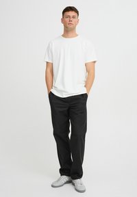 Hvid bomulds-T-shirt parret med sorte bukser. Modellen har grå sneakers på. Sættet har en enkel, afslappet pasform og minimalistisk design.