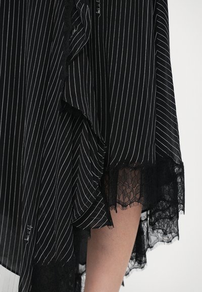 Tejido negro con rayas verticales blancas presenta un volante a lo largo del borde destacado por detalles de encaje negro. Textura ligera y fluida.