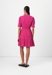 Fuchsia jurk met korte puffmouwen, gerimpelde halslijn, aansluitende taille en uitlopende rok. Inclusief decoratieve stiksels aan de zoom.