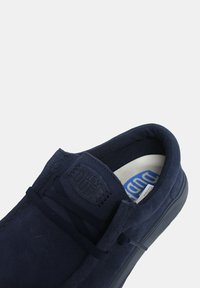 Zapato de ante azul marino con punta redondeada, textura suave y cordones a tono. Presenta un parche de logo en la lengüeta y una suela de contraste.