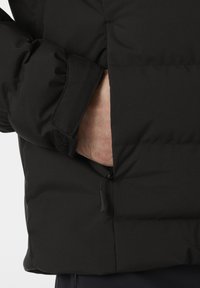 Schwarze isolierte Jacke mit gestepptem Design, Reißverschlusstasche und Klettverschluss am Ärmel. Der Stoff hat eine glatte Textur.