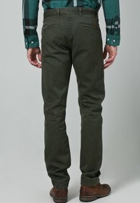 Ciemnozielone spodnie o dopasowanym kroju, wykonane z bawełny. Posiadają dwie tylne kieszenie, subtelne szwy i są zestawione z brązowymi butami.