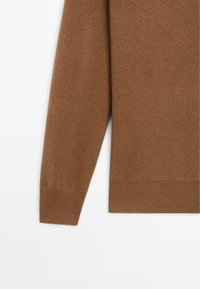 Hnědý pletený svetr s hladkou texturou, má dlouhé rukávy a ribbovaný lem. Design je jednoduchý a klasický, bez vzorů.