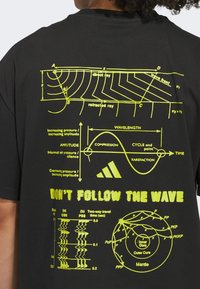 Zwarte t-shirt met gele wetenschappelijke diagrammen en de tekst "VOLG DE Golf NIET", met verschillende illustraties van golven en druk.