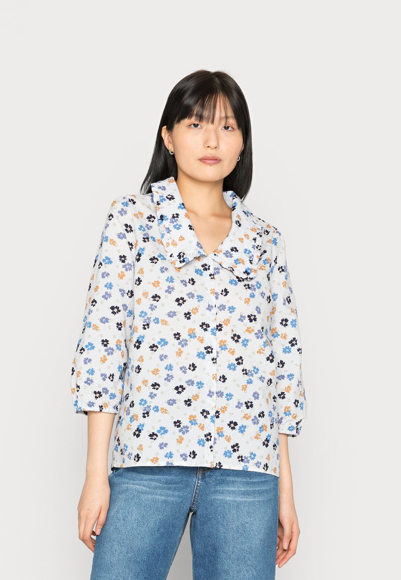 Camisa de botão floral em tecido leve com padrões em azul, laranja e preto. Apresenta um colarinho grande e mangas três quartos.