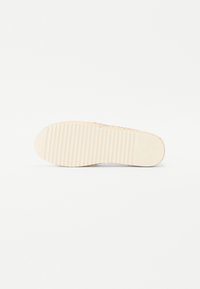 Sko såle med en strukturert, rillede mønster i lys beige, laget av gummi, designet for grep og holdbarhet, med en jevn kant.