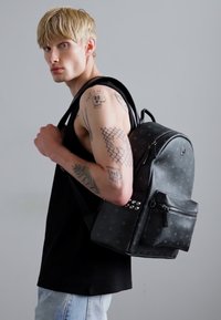 Musthave mustakott, mis on valmistatud tekstuuriga materjalist, millel on nurgad ja esikott, kandes mudelit heledate juustega.