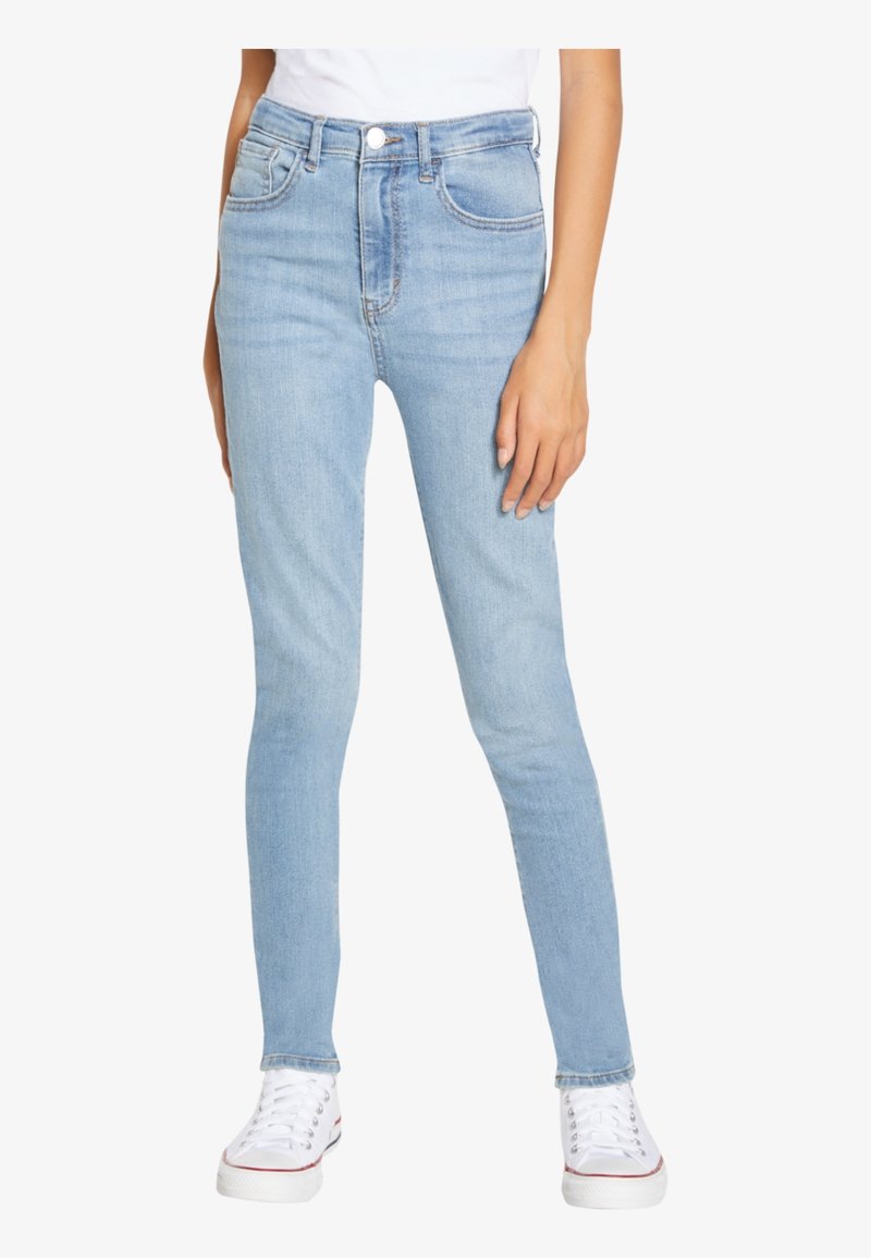 Light blue skinny jeans with a high waist, featuring front pockets and a button fly, paired with white sneakers. Smooth denim texture.