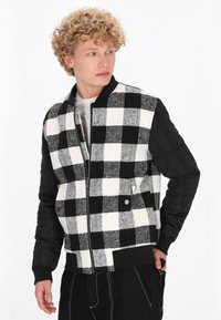 Czarna i biała bomberka w kratę z miękkim wełnianym przednim panelem i gładkimi czarnymi rękawami. Posiada zamek błyskawiczny i zatrzaski.