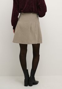 Gonna a pieghe a scacchi bianco e nero con design a campana. Indossata con un maglione borgogna a trama e collant neri, abbinata a stivaletti.