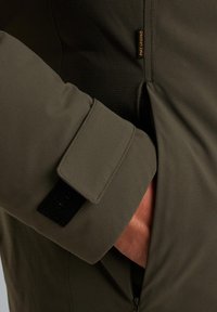 Olivengrøn jakke med en tekstureret stof, justerbare ærmer med Velcro-lukning og synlig lynlås lomme detalje.
