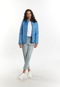 Jachetă pufosă bleu deschis, cu quilt-ing orizontal, asortată cu un pulover alb cu nervuri și blugi bleu deschis. Tenisi albi cu accente colorate.
