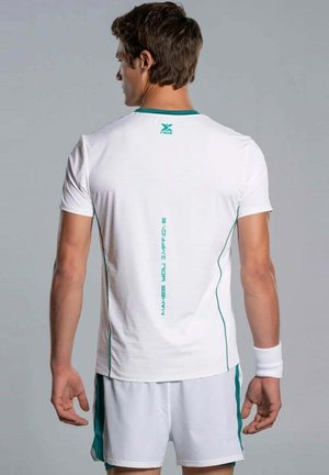 Man in witte sportkleding, met de rug naar de kijker, draagt een polsbandje en een shirt met verticale tekst "MAKES YOU IMPROVE" op de achterkant.