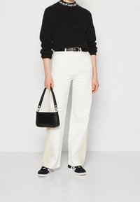 Czarny sweter z prążkowanej dzianiny, białe spodnie z szerokimi nogawkami, czarny pasek, mała czarna torebka oraz czarne trampki z białymi podeszwami i paskami.