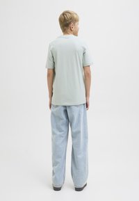 Ljusgrön kortärmad t-shirt i kombination med baggy ljusblå jeans, med en avslappnad passform och avslutade med svarta skor.