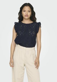 Top blu navy con design a fiori ritagliato, maniche a volant, scollatura rotonda, abbinato a pantaloni alti color crema.