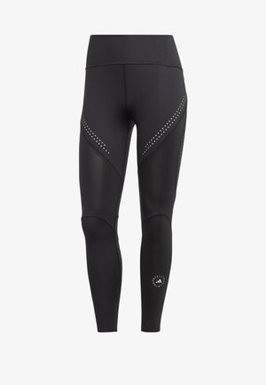 Black athletic leggings with mesh panels and dot accents, featuring a high waistband and a logo at the lower leg. Smooth, stretchy material.