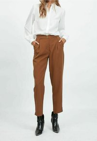 Ruske sopere pantalone s visokim strukom, nabranim detaljima i bočnim džepovima, uparenim s belom bluzom dugih rukava i crnim čizmama do gležnja.