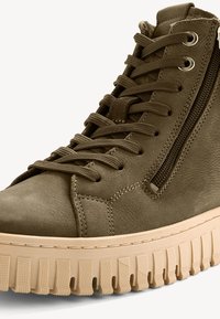Bottines montantes en cuir vert olive avec surface texturée, lacets ton sur ton et une fermeture à glissière sur le côté ; elles sont dotées d'une semelle en caoutchouc beige épaisse.