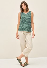 Top verde senza maniche con motivo a onde, scollatura a V, abbinato a pantaloni cropped beige chiaro e sandali verde con fibbia.