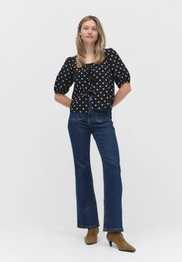 Svart blus med prickar, puffärmar och frontknut, ihop med mörkblå utsvängda jeans och bruna ankelboots. Enkelt mönster, klassisk passform.
