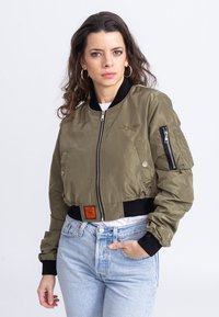 Giacca bomber verde oliva con design cropped, chiusura con zip, polsini neri a coste e tasche laterali. Presenta un'etichetta arancione del marchio in vita.