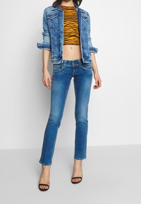 Jeansjacka och kort tigerrandig topp i kombination med blå smalpassade jeans och svarta klacksandaler. Funktioner inkluderar knappar och sömnadsdetaljer.