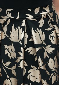 Μαύρη υφασμάτινη φούστα με πλισέ σχεδιασμό, διακοσμημένη με μεταλλικά χρυσά λουλουδένια μοτίβα. Ομαλή υφή με αντιθετικά χρώματα και κομψές λεπτομέρειες.