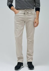 Pantalones de mezcla de algodón beige con cintura ajustable, dos bolsillos laterales y corte slim, combinados con zapatillas deportivas negras.