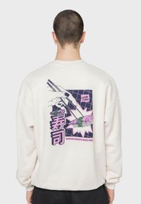 Sudadera color crema con un estampado gráfico de sushi con palillos, detalles morados y el texto "¡HORA DE SUSHI!" y "寿司".