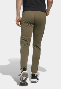 Olijfgroene sportbroek met een tapering fit, voorzien van zwarte zijstrepen, een zachte textuur en gecombineerd met zwarte sportschoenen.