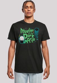 Zwarte t-shirt met kleurrijke grafische print met de tekst "Meester van de Donkere Kunsten," cartoonfiguren en abstracte ontwerpen in groen en blauw.