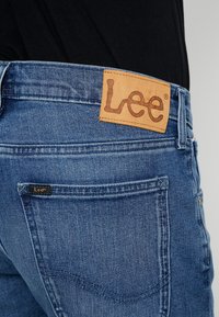 Světle modré denimové džíny s koženou nášivkou značky Lee na pase, s klasickými zadními kapsami a jemnými švy.