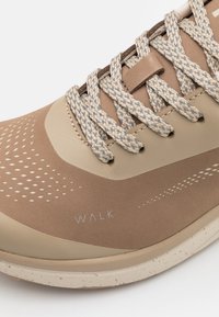 Jasnobrązowy but sportowy z gładką cholewką w kropki, teksturowanymi sznurówkami i białym logo "WALK" po boku.