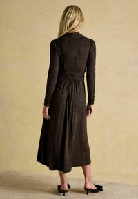 Schwarzes langärmeliges Kleid mit geraffter Taille und Leopardenmuster. Fließende Midi-Länge mit glatter Textur, kombiniert mit schwarzen Absatzmules.