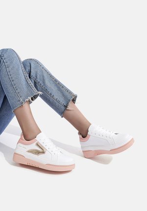 Sneaker bianchi con accenti rosa, caratterizzati da un dettaglio laterale dorato lucido, suola testurizzata e design con lacci, abbinati a jeans di jeans sfrangiati.