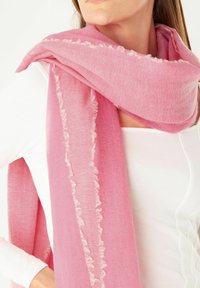 Rosa Schal aus weichem Stoff, mit Fransenverzierungen an den Kanten, um den Hals drapiert, kombiniert mit einem weißen Oberteil.