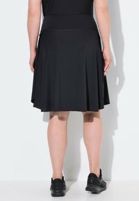 Zwarte skaterrok met een aangesloten tailleband, geplooid ontwerp en knielengte. Gecombineerd met zwarte sportschoenen.