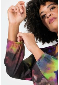 Blusa fluida de base negra, con un vibrante patrón en acuarela en tonos púrpura, verde y rosa. Los puños elásticos acentúan las mangas.