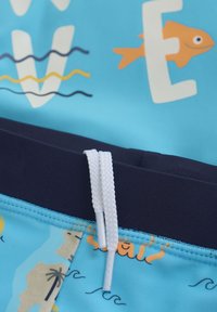 Blå simshorts med en korallfiskgrafik och vågmönster. Har en marinblå midja med vit dragsko och texturerad tyg.