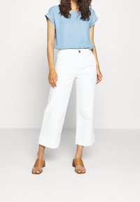 Ljusblå kortärmad topp, vita vida byxor med uppvikta fållar och tanfärgade slidesandaler med blockklack. Enkel, ren design.