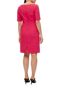 Robe courte rose avec des manches courtes, fermeture éclair au dos et fente arrière. Le tissu est lisse et la silhouette est cintrée.