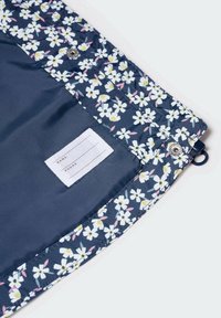 Floral-patterned fabric with white daisies on a dark blue background. Includes a cotton label for name and phone details. Silver snap closure.