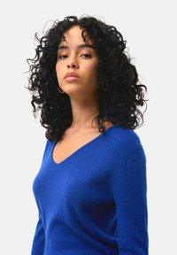 V-Ausschnitt-Pullover in lebhaftem Blau, aus weichem Material. Mit verlängerten Ärmeln und lockerer Passform, die eine glatte Textur zur Schau stellt.