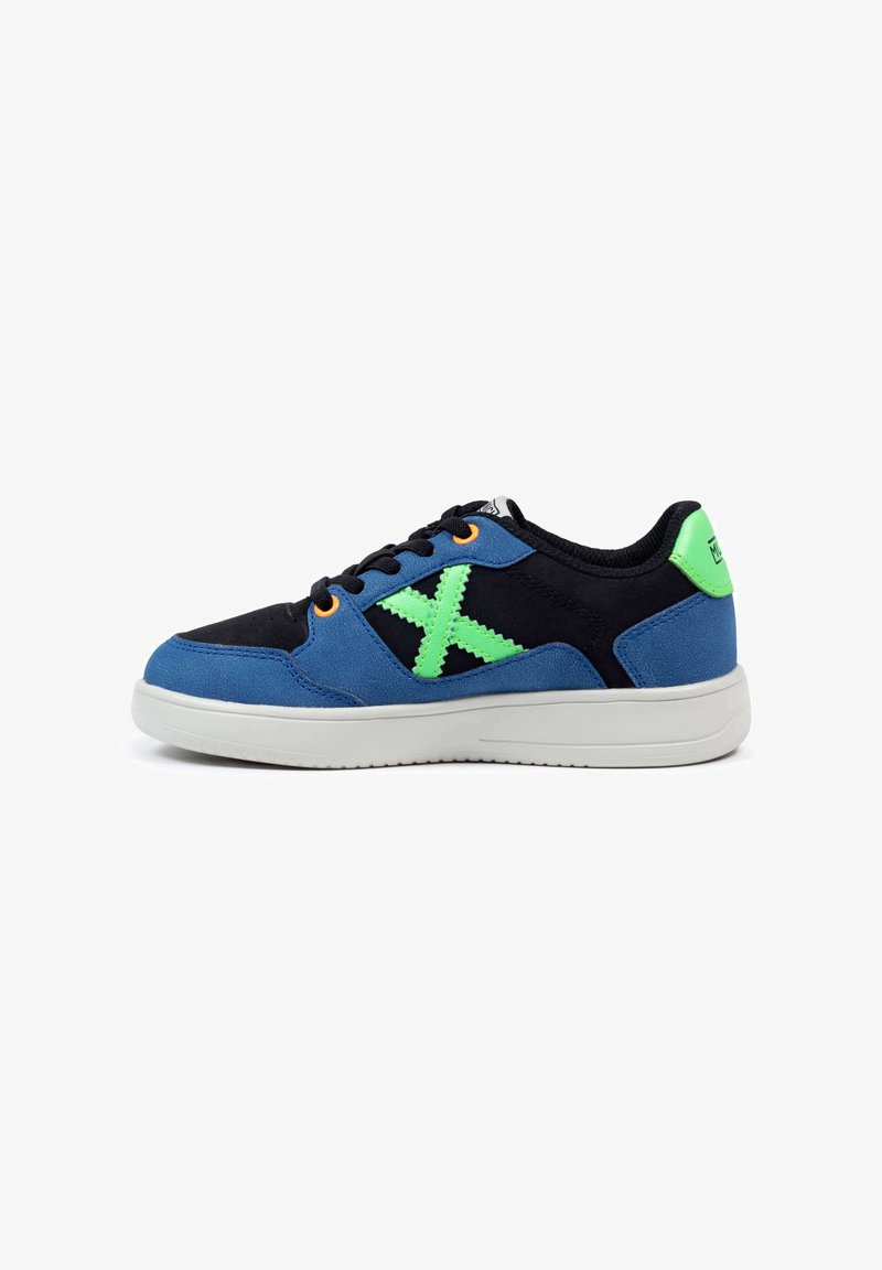 Zapatillas de ante azul y negro con un acento geométrico verde y ojales naranjas. Presenta una suela de goma blanca y un cuello acolchado.