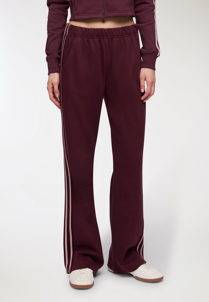 Bordowe dresy o szerokim kroju, z białymi paskami po bokach i elastycznym pasem. Wykonane z miękkiego materiału, z kieszeniami.