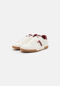 White sneakers with a rubber sole, featuring a maroon accent stripe, textured toe cap, and lace-up closure. Smooth synthetic material.